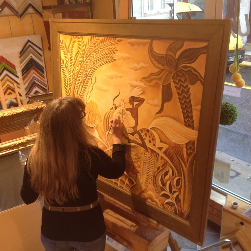 Photo d'une vue dans l'atelier où Mme Lantrès intervient sur un grand tableau orientaliste aux teintes jaunes, stylisé, représentant une cavalière entrain de chasser